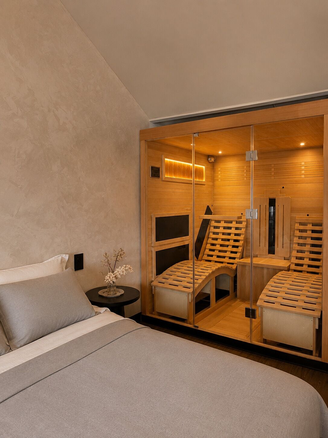 A modern bedroom with a large bed, a nightstand, a small table with a vase, and a sliding glass door leading to a sauna area.