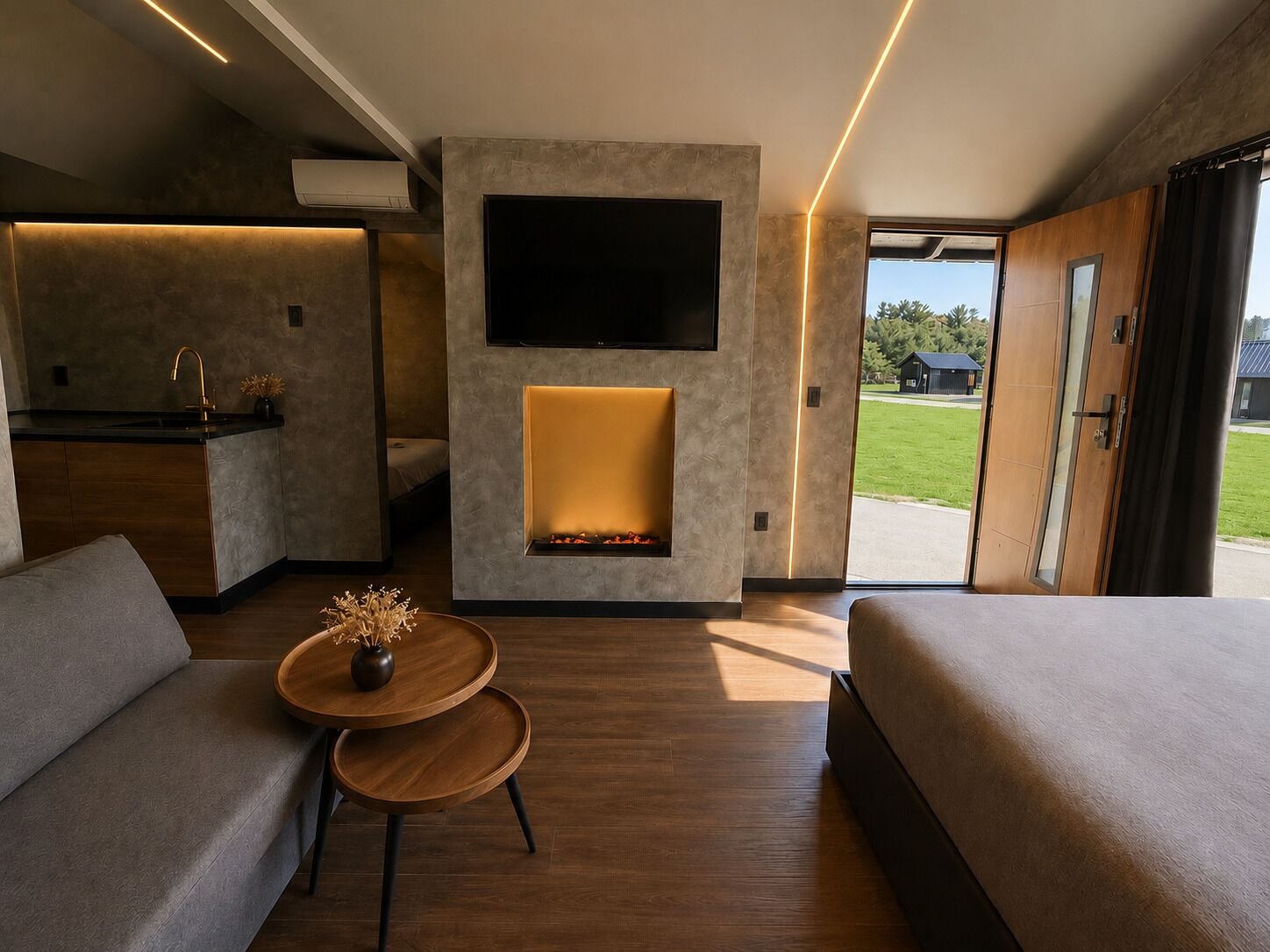 Una habitación de hotel moderna con un sofá, una mesita con un florero, una chimenea, un televisor y vistas al exterior.