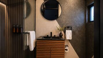 A modern bathroom with a wooden vanity, a round mirror, and a glass shower enclosure.