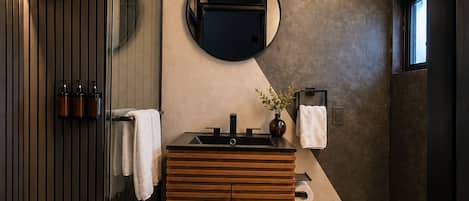 A modern bathroom with a wooden vanity, a round mirror, and a glass shower enclosure.