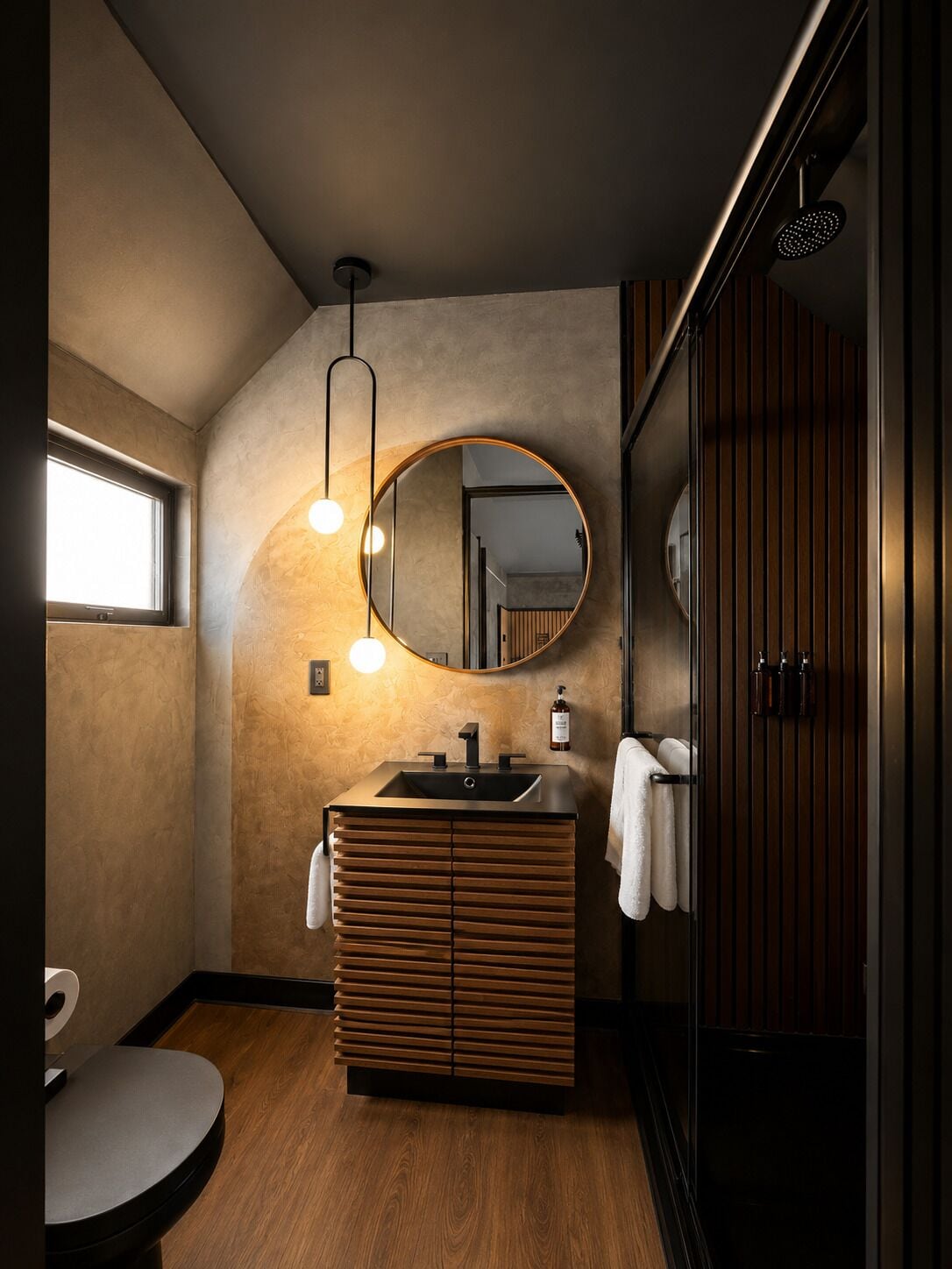 A modern bathroom with a wooden vanity, a round mirror, and a shower enclosure.