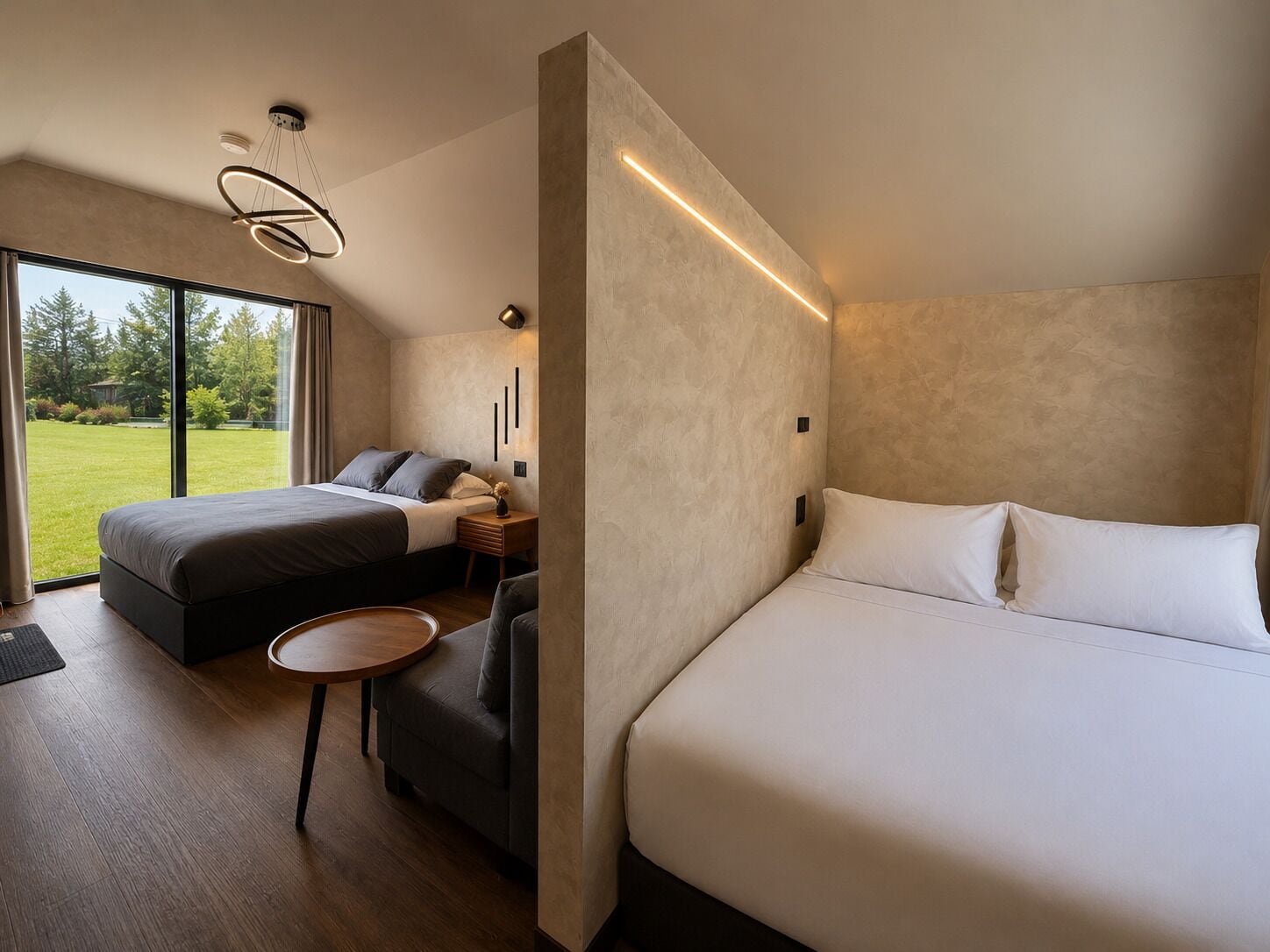 A modern bedroom with a large bed, a smaller bed, a round table, and a view of a green landscape.