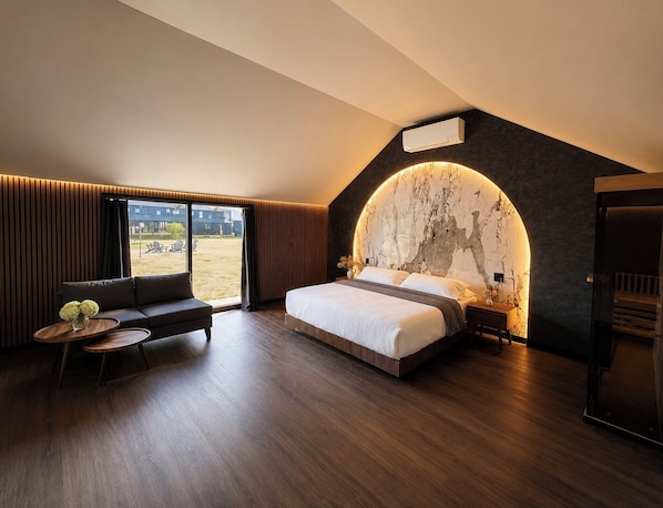 A modern bedroom with a large bed, a seating area, and a view of the outdoors. - Emrose Luxury Cabins (Brandon)