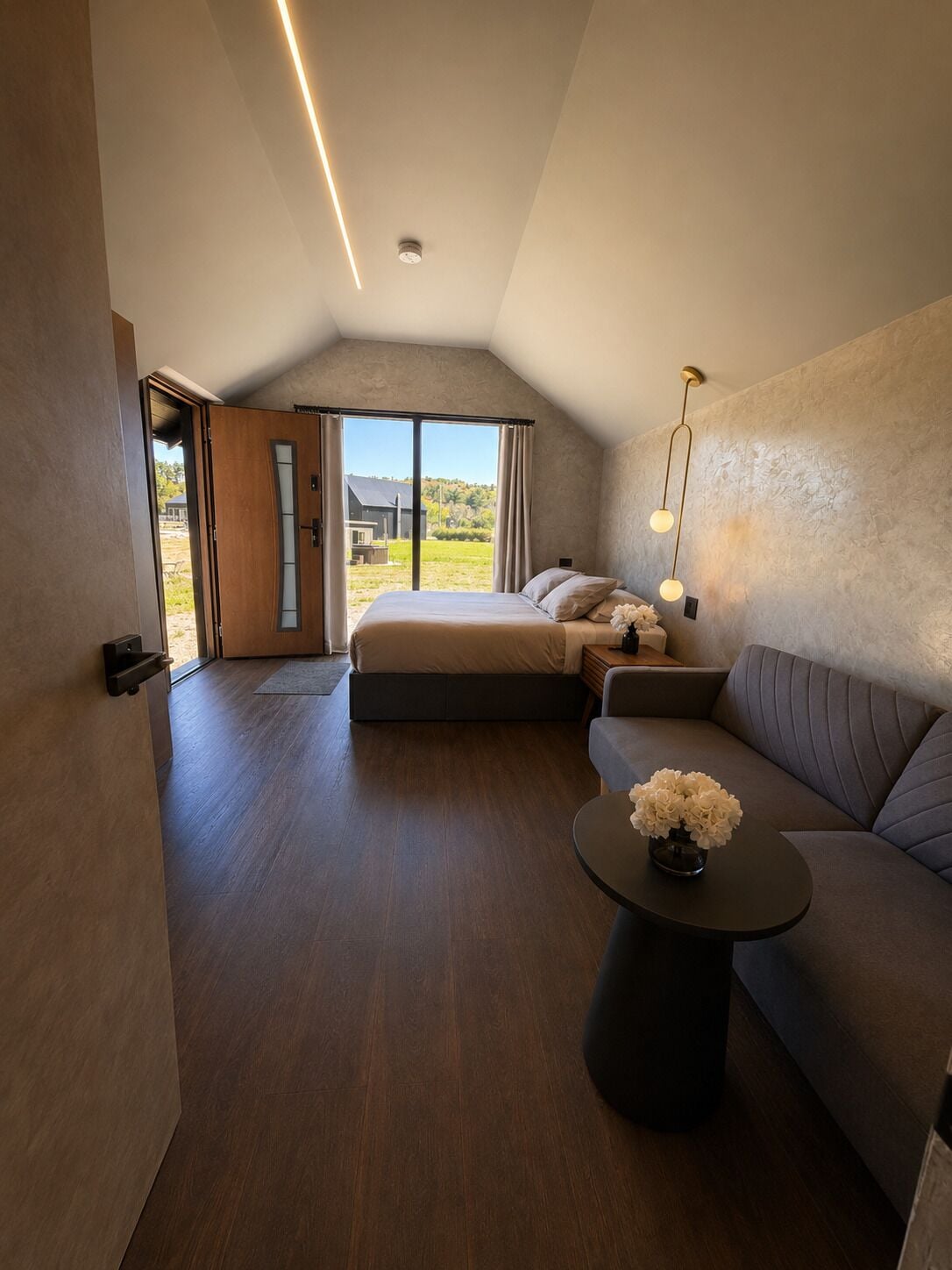 Un dormitorio con cama, sofá, una mesita con flores y vistas al exterior.