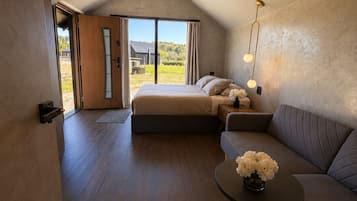 A bedroom with a bed, a sofa, a small table with flowers, and a view of the outdoors.