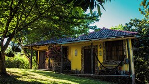 Une maison jaune avec un toit en tuiles, une véranda et un hamac.