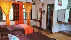 Une chambre avec deux lits, un plafond en bois, un appareil de climatisation, une petite étagère et une porte donnant sur une autre pièce.