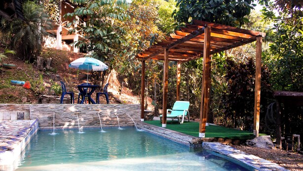 Une piscine agrémentée d’une pergola en bois, de deux chaises bleues et d’une chaise longue verte.