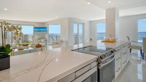 Cozinha moderna com bancada de mármore, forno embutido e vista para o mar.
