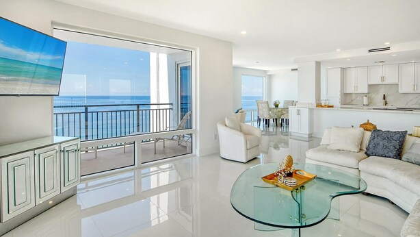 Uma sala de estar moderna com uma mesa de centro de vidro, sofás brancos e vista para o oceano.