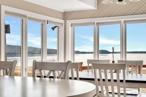 A dining area with a large table and chairs, large windows with a view of a body of water and distant land. - Lakeside Retreat on Saratoga Lake (Saratoga Springs)