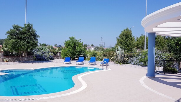 Une piscine à l’eau bleue, entourée d’une terrasse blanche et de chaises longues bleues.