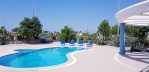 Ein Swimmingpool mit blauem Wasser, umgeben von einer weißen Liegefläche und blauen Liegestühlen.