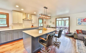 A modern kitchen with a central island, bar stools, and a dining area with a view. - Modern Retreat | Near Hunter & Windham | Dog-Friendly (Jewett)