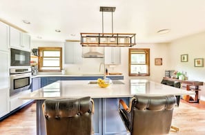 A modern kitchen with a central island, white cabinets, and a dining area with leather chairs. - Modern Retreat | Near Hunter & Windham | Dog-Friendly (Jewett)