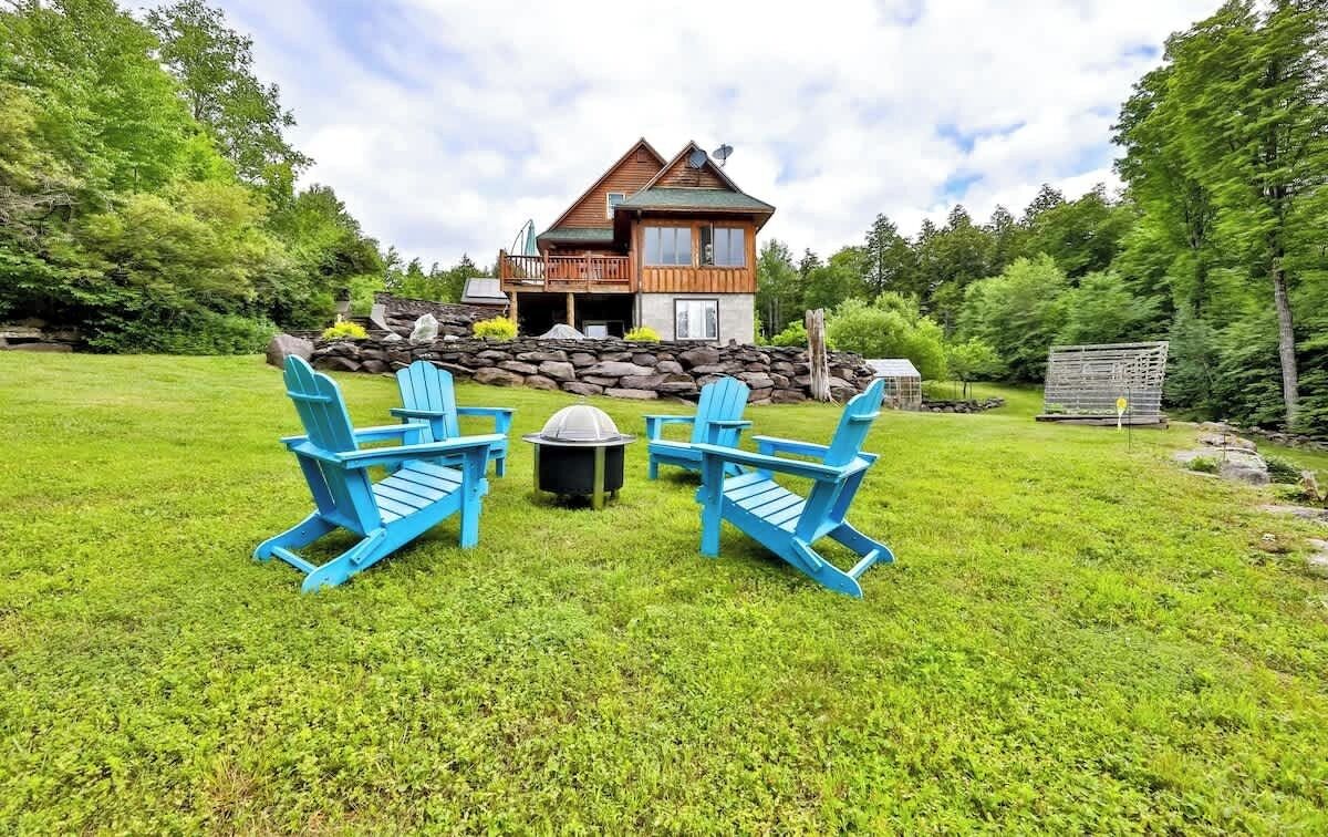A wooden house with a stone foundation, surrounded by a grassy lawn and trees.