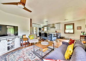 A modern living room with a sofa, coffee table, and a dining area with chairs and a kitchen in the background. - Modern Retreat | Near Hunter & Windham | Dog-Friendly (Jewett)