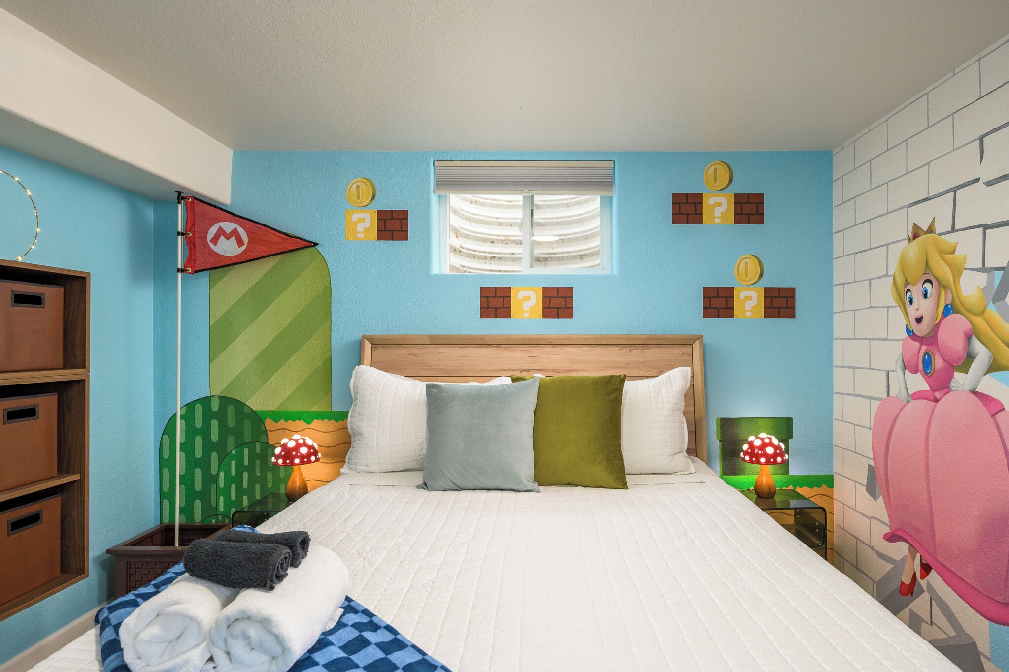 Une chambre à coucher avec un lit, des oreillers, une table de chevet, une lampe, une fenêtre et un mur orné de points d’interrogation et d’un drapeau.