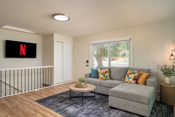 A modern living room with a grey sofa, a round coffee table, and a flat-screen TV mounted on the wall. - Mini Golf • Fire Pit • Hot Tub, Game House for 14 (Arvada)