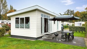 A small, single-story mobile home with a patio area, a grill, and an umbrella. - Amazing home in Heinkenszand with WiFi (Heinkenszand)