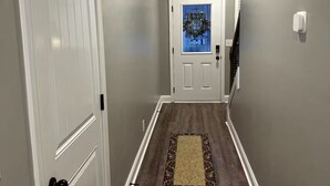 Un pasillo con una puerta blanca, una puerta de vidrio con vista a la ciudad y una alfombra estampada en el suelo.