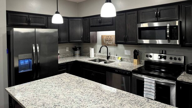 Una cocina moderna con armarios oscuros, electrodomésticos de acero inoxidable, encimeras de granito e iluminación colgante.