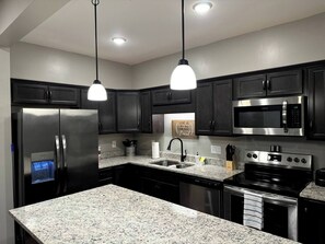 A modern kitchen with dark cabinets, stainless steel appliances, granite countertops, and pendant lighting. - Beautiful Townhome with Pool (Clarksville)