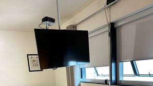 Een hotelkamer met een bed, een grijze bank, een flatscreen televisie en een raam met gordijnen.