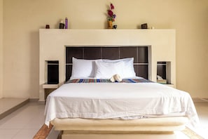 A neatly made bed with white linens and a colorful blanket, a headboard with a dark panel, and a vase with flowers on the nightstand.