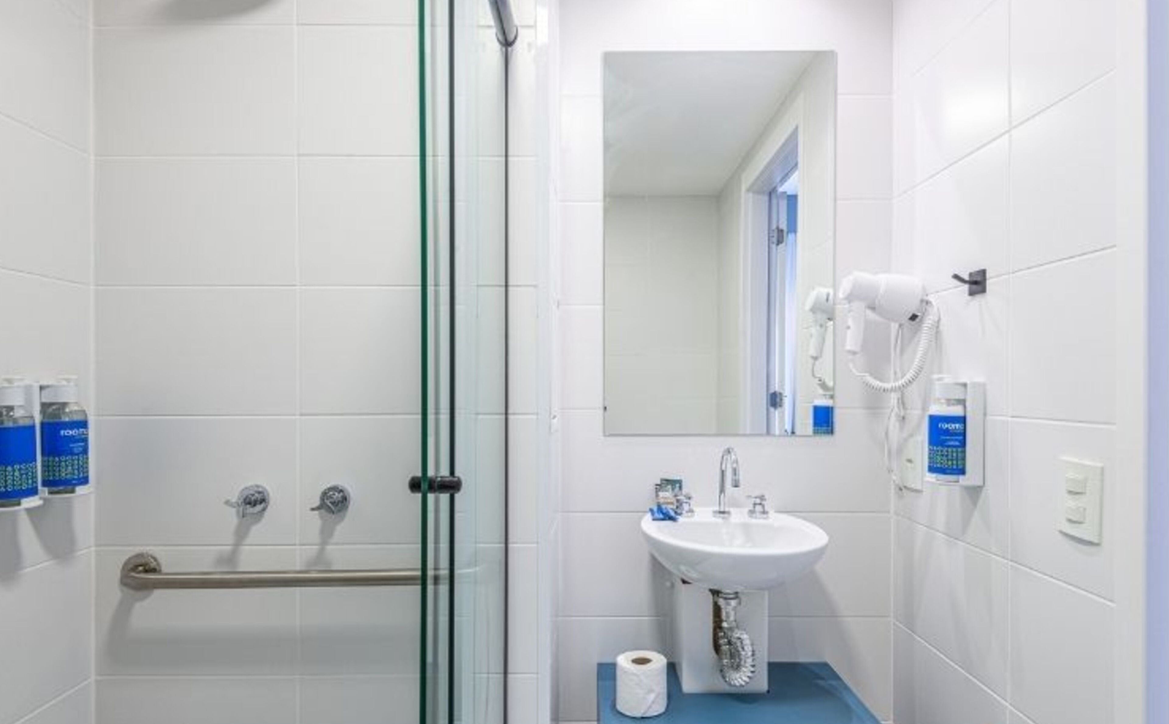 Une salle de bain avec une douche à parois de verre, un lavabo avec un miroir au-dessus et des articles de toilette fixés au mur.