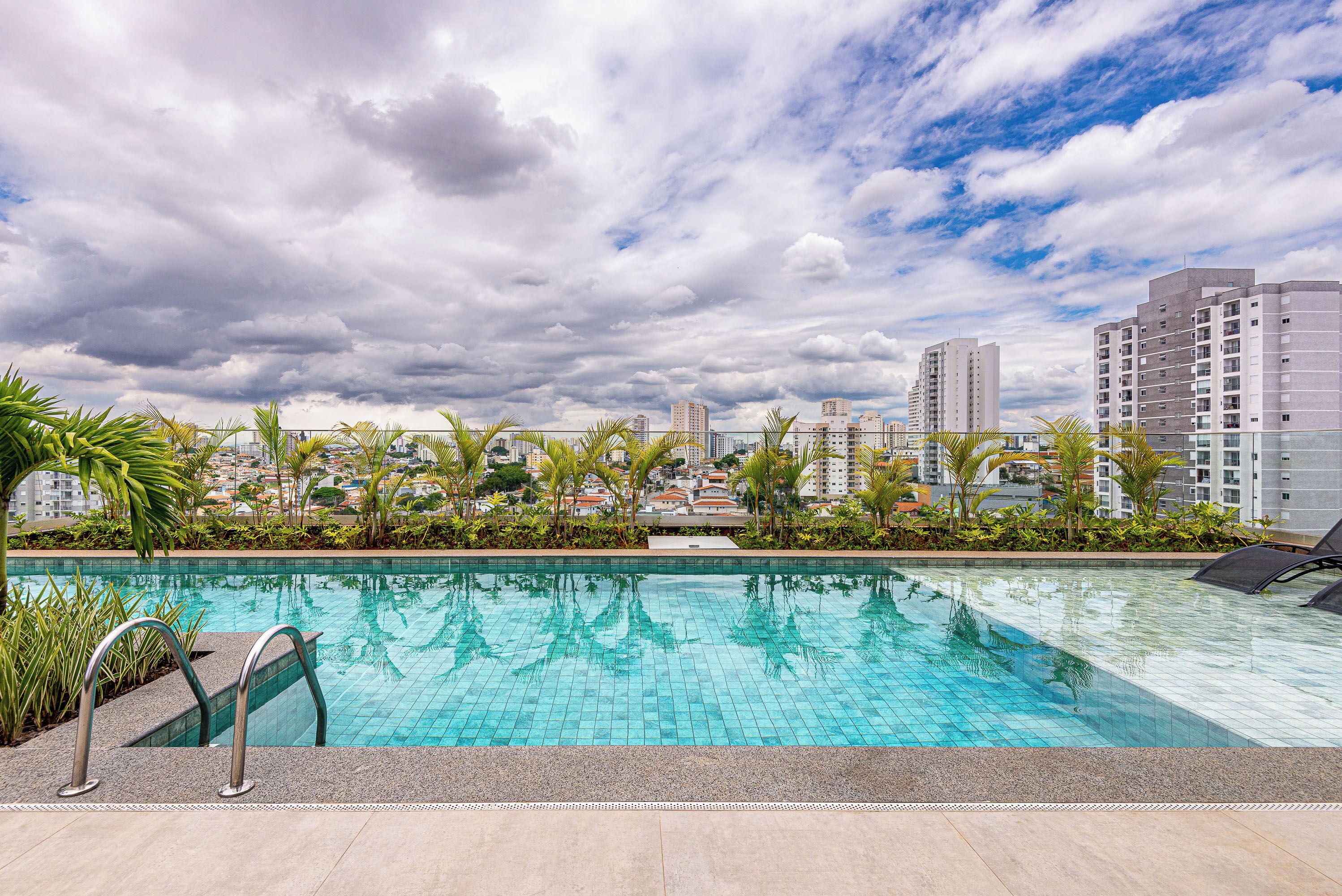 Una piscina en la azotea con vista a un paisaje urbano, rodeada de palmeras y edificios modernos.