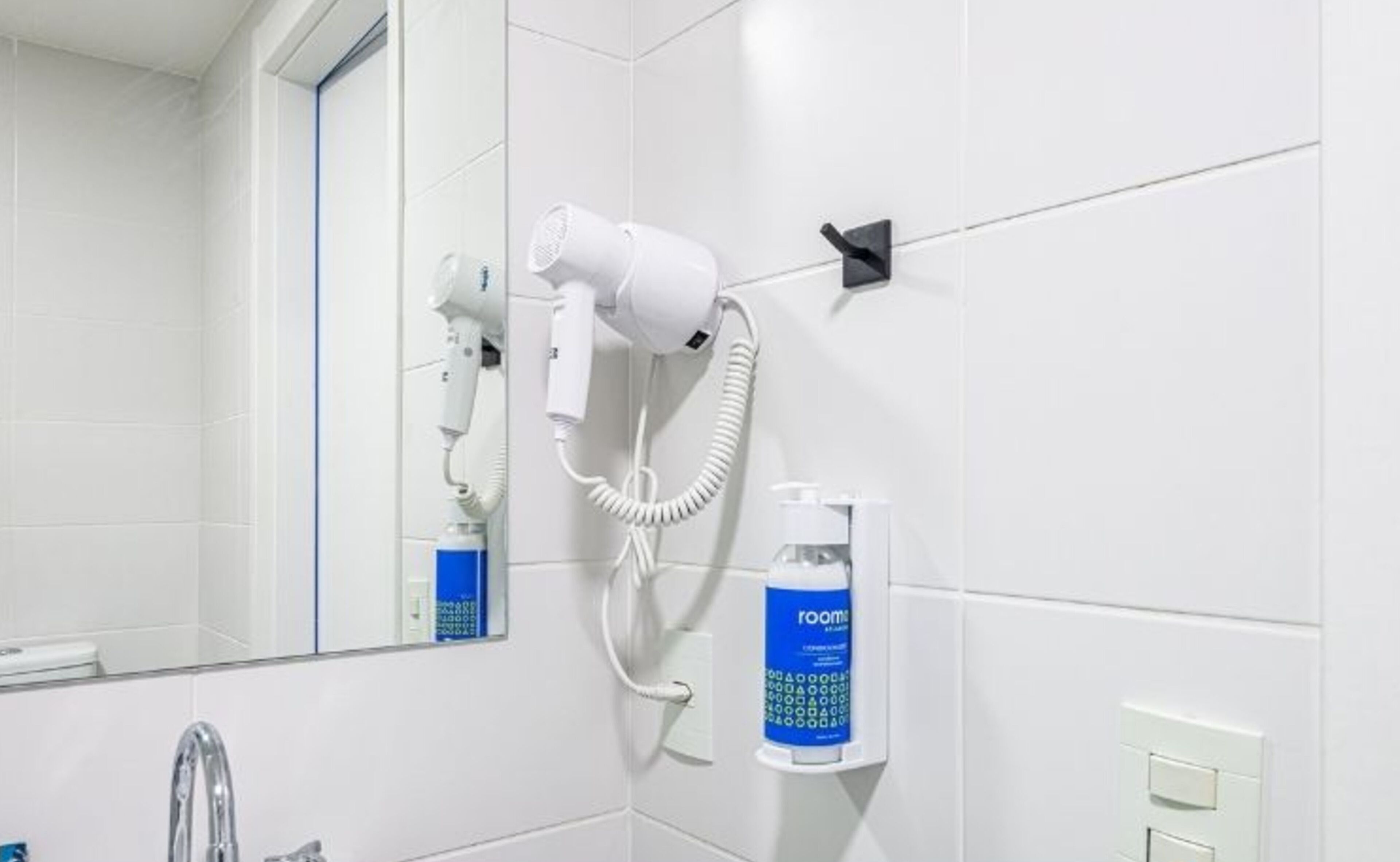 Une salle de bain équipée d’un sèche-cheveux fixé au mur, d’un miroir et d’un vaporisateur d’ambiance.