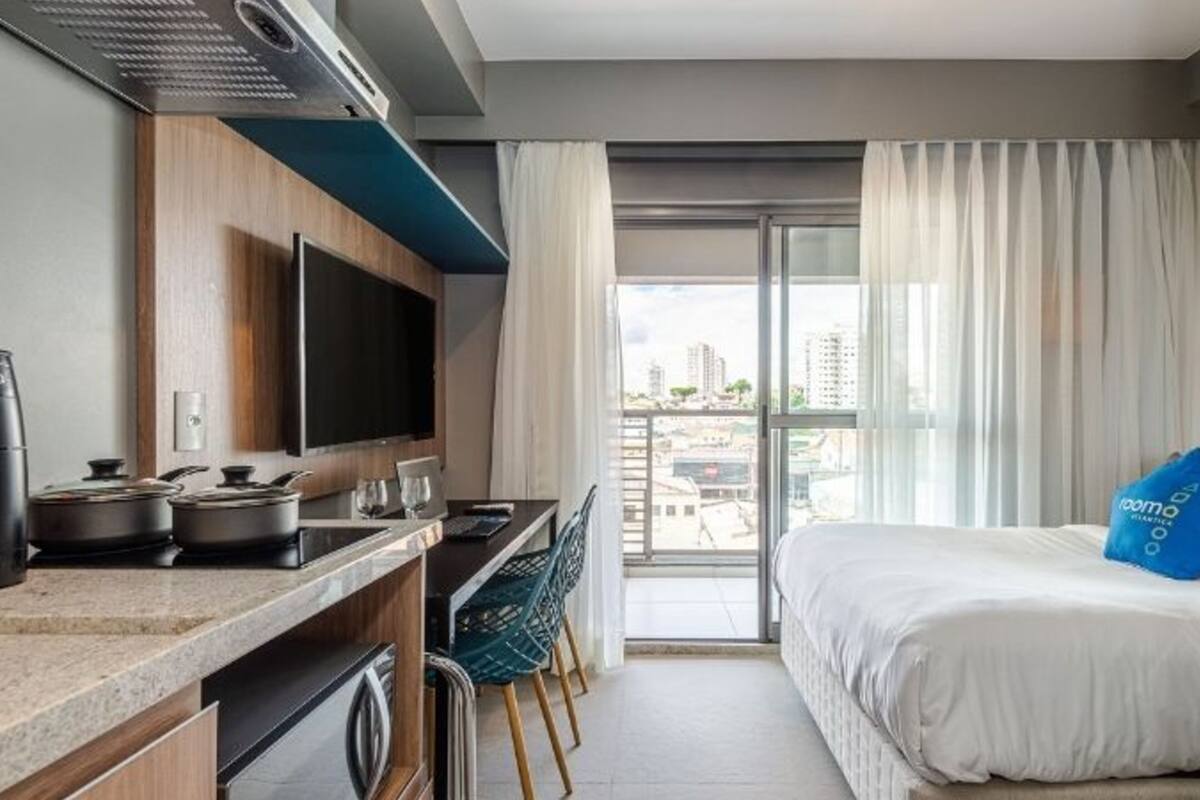 A modern hotel room with a kitchenette, a bed, and a view of the city.