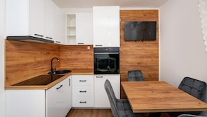 A compact kitchen with white cabinets, a wooden countertop, a built-in oven, and a dining area with a wooden table and chairs.