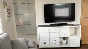 Un salon moderne avec un canapé gris, une table basse blanche et un téléviseur posé sur un meuble blanc.