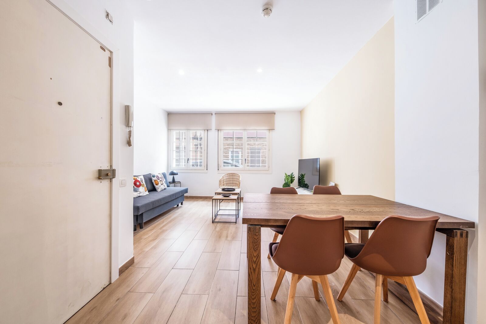 A modern living room with a sofa, a dining table with chairs, and a TV.