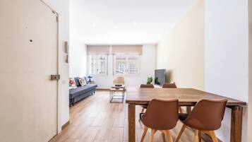 A modern living room with a sofa, a dining table with chairs, and a TV.
