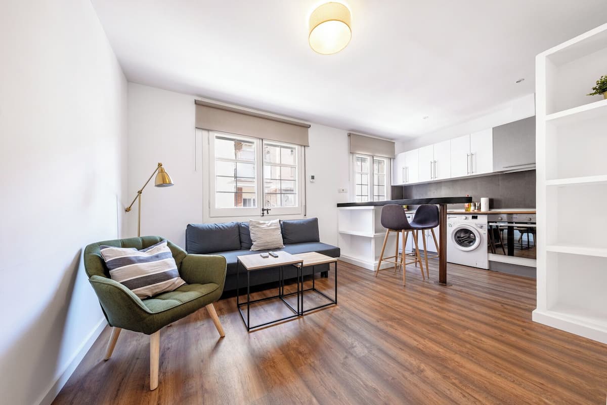 Un appartement moderne comprenant un fauteuil vert, un canapé, une table à manger et un coin cuisine avec un lave-linge.
