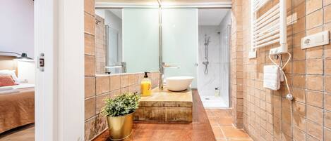 A bathroom with a wooden vanity, a large mirror, a white sink, and a shower area.