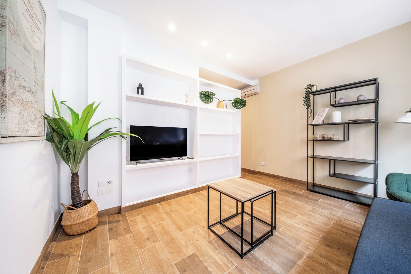 Un salon moderne doté d’un téléviseur à écran plat, d’un parquet, d’une table basse, d’une plante en pot et d’une bibliothèque.