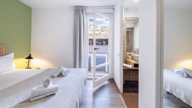 Une chambre d’hôtel avec deux lits, une salle de bain avec un miroir et une vue sur la ville, visible à travers une porte vitrée.
