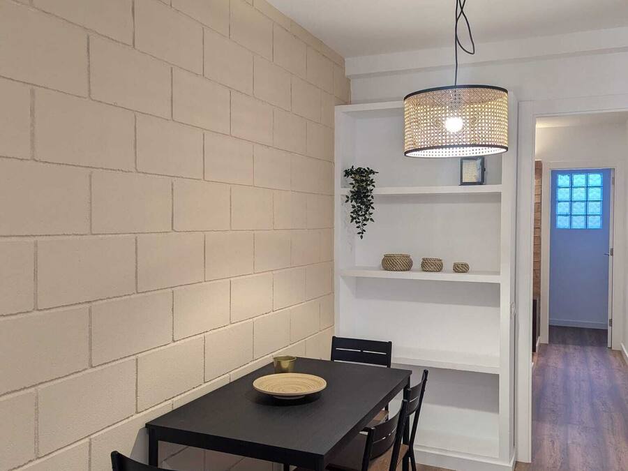 A dining area with a brick wall, a black table, and chairs. There is a hanging light fixture above the table.