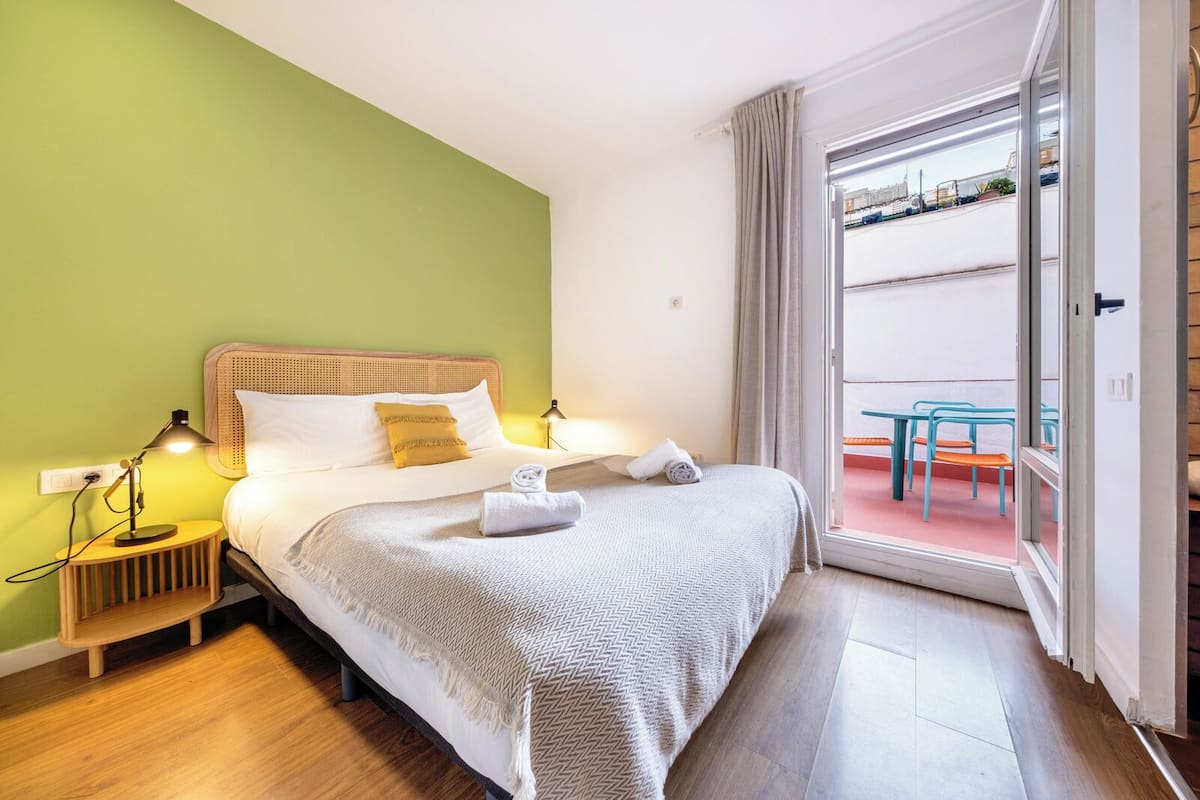Une chambre d’hôtel avec un lit, des lampes de chevet, une petite table d’appoint en bois et une vue sur le balcon extérieur.