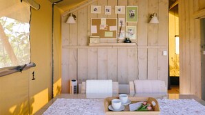 Een gezellige kamer met houten inrichting, een tafel met kantkleed, een dienblad met kopjes en tulpen, en een prikbord met foto’s en notities.