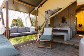 A cozy outdoor seating area with a wooden bench, a cushioned sofa, and a small table with a vase of flowers.