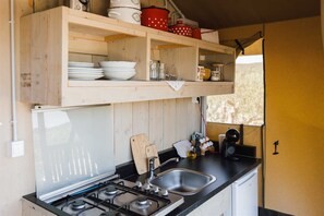 Une cuisine compacte équipée d’une cuisinière à gaz, d’un évier et d’étagères en bois au-dessus, où sont rangés la vaisselle et les ustensiles de cuisine.