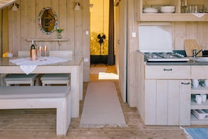 A wooden interior with a dining table, a kitchen area with a stove, and a mirror with a floral frame.