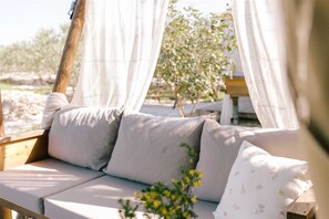 A wooden bench with a cushioned seat and backrest, draped with sheer white curtains.