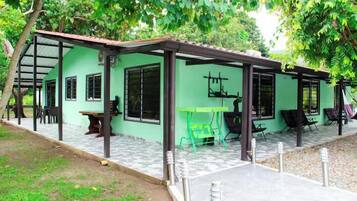 A green building with a covered patio area, outdoor seating, and a small table.