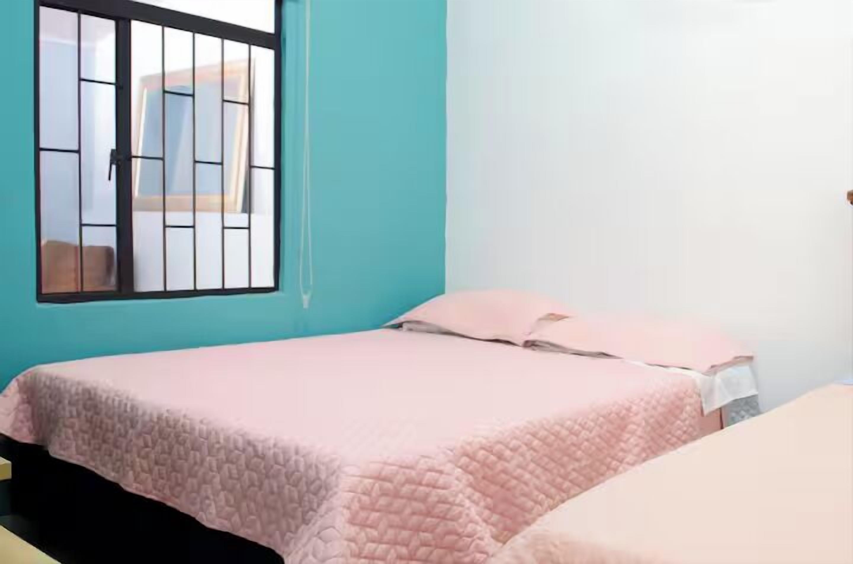 A room with a bed, a window with bars, and a teal wall.